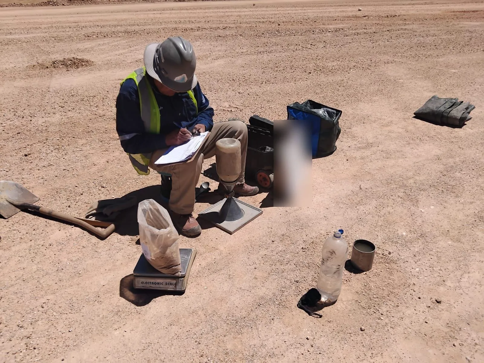 Técnico registrando datos junto al equipo de densidad en sitio, en un terreno de tierra.
