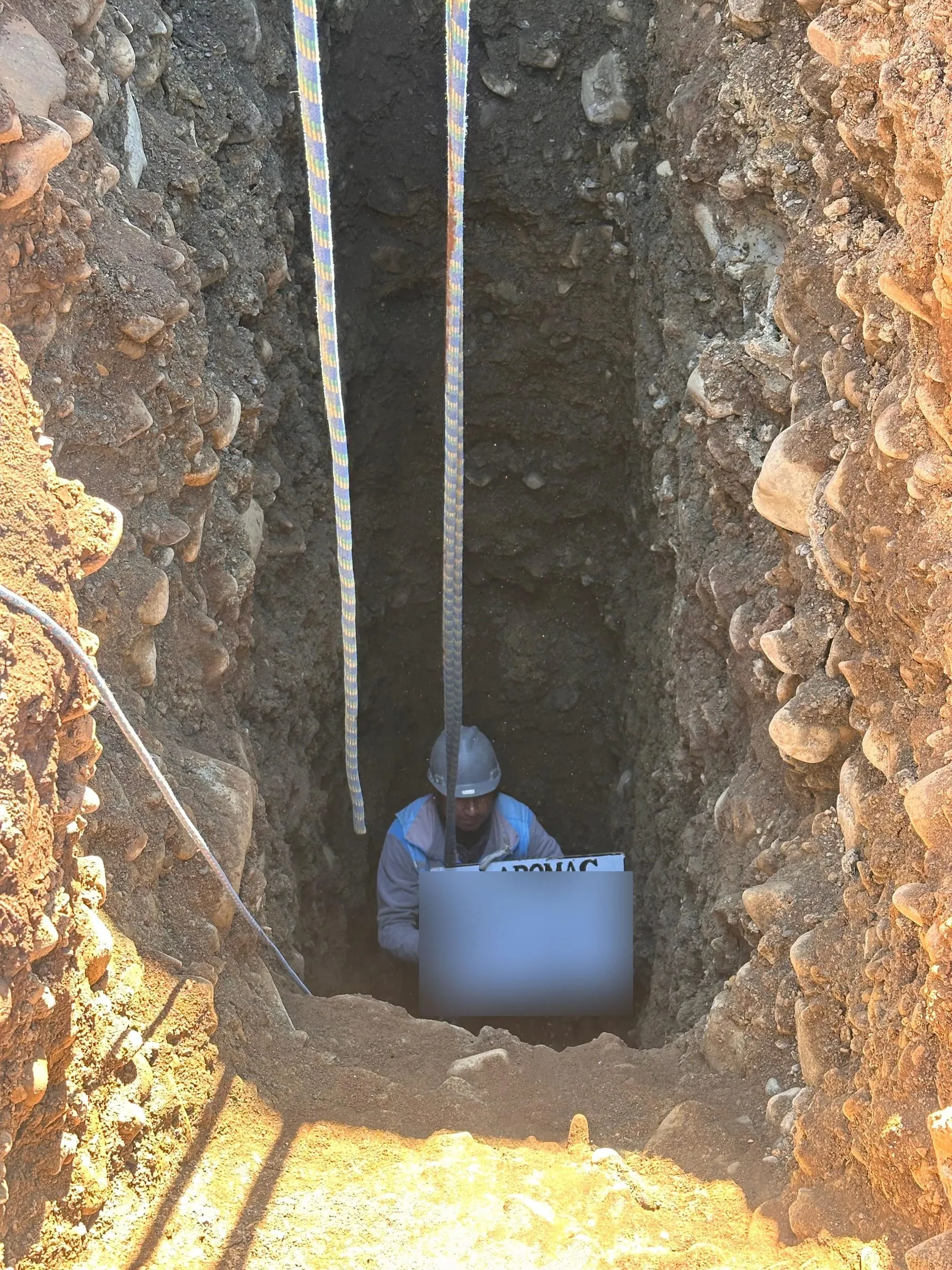 Técnico dentro de un pozo de exploración profundo, sosteniendo la pizarra de identificación de la muestra.