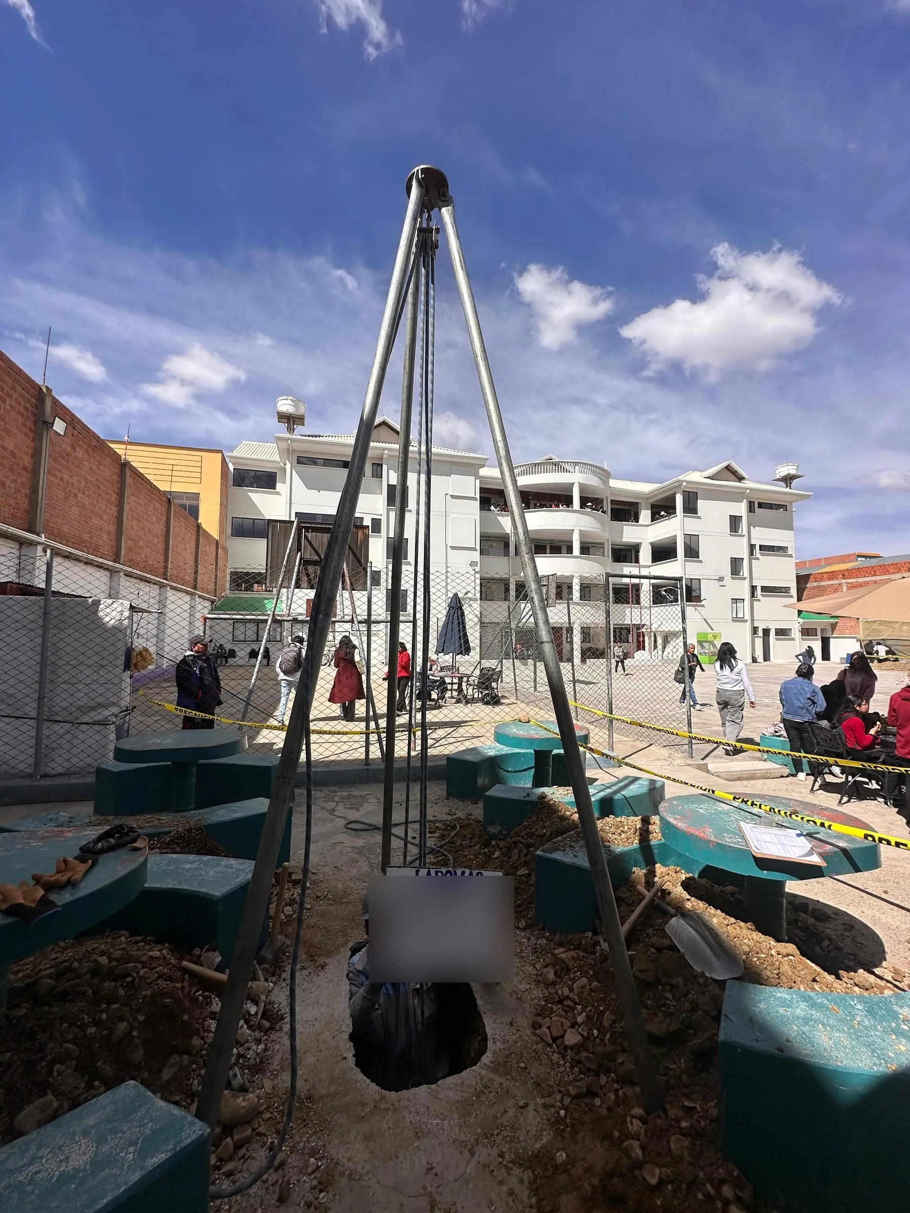 Trípode metálico sobre un pozo de exploración en un patio urbano, con un edificio al fondo.